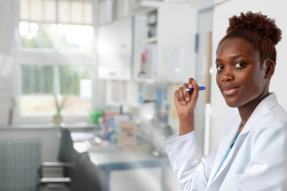 A woman in a lab coat standing in a lab holding a pen
